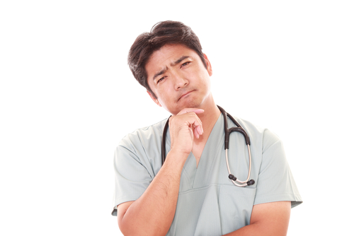 Un médecin en uniforme médical penche la tête sur le côté en portant une main à son visage, l’air confus.