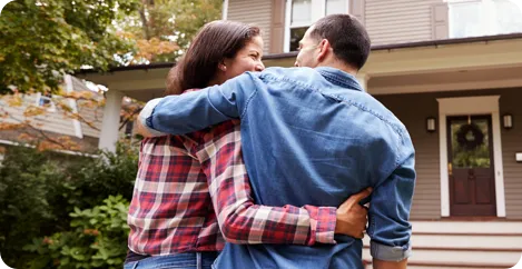 A couple hugs each other in front of their new home.