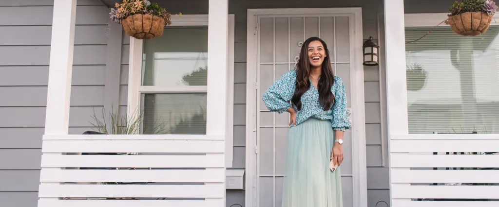 A woman smiles as she stands on the front porch of her new home