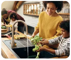 Une mère et son fils lavent des fruits et légumes dans leur évier de cuisine