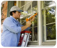 Un homme colmate des fissures autour des fenêtres d’une maison