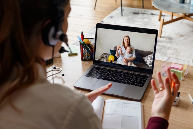 A person participates in a virtual care appointment, viewing a doctor on a laptop screen as the doctor speaks and gestures during the video consultation.