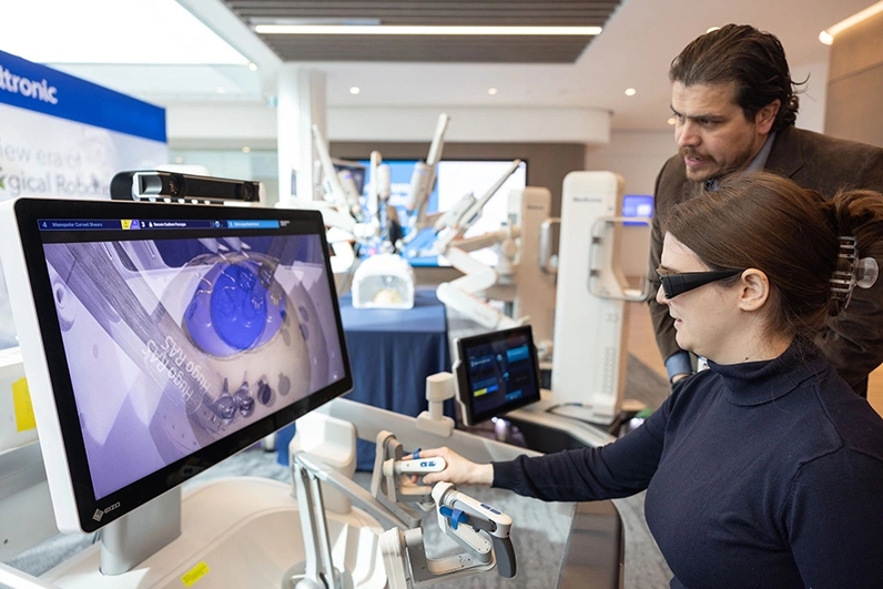 Une femme essaie une station de démonstration de robot chirurgical lors de l’événement L’avenir des soins de santé de BMO, tandis qu’un homme lui offre des conseils. 