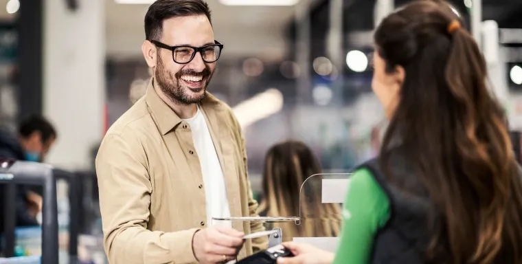 A person pays at a checkout counter, holding out a card while a cashier processes the transaction, representing the ability to use points directly toward eligible purchases.