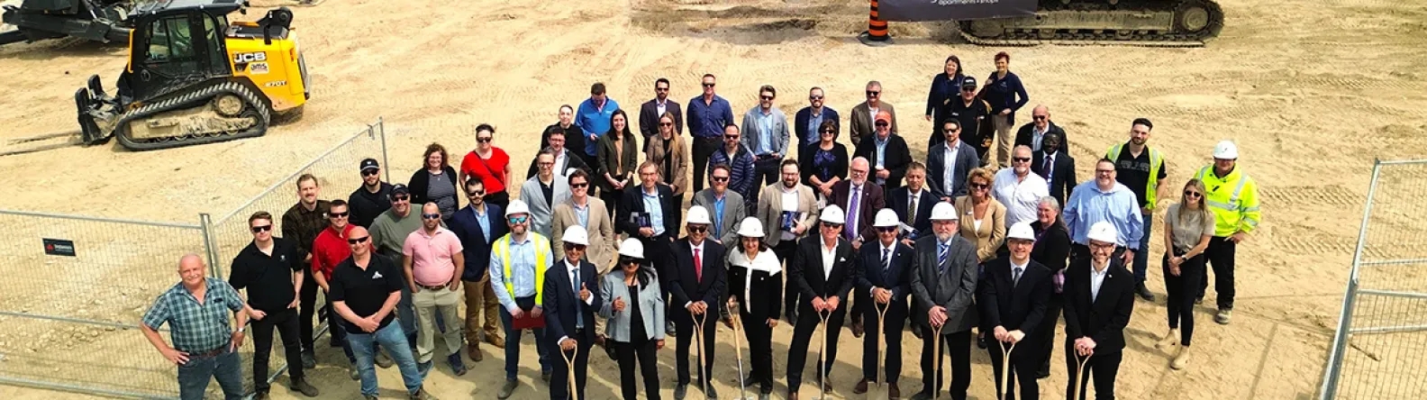 A group of people in hardhats breaking ground at a construction site