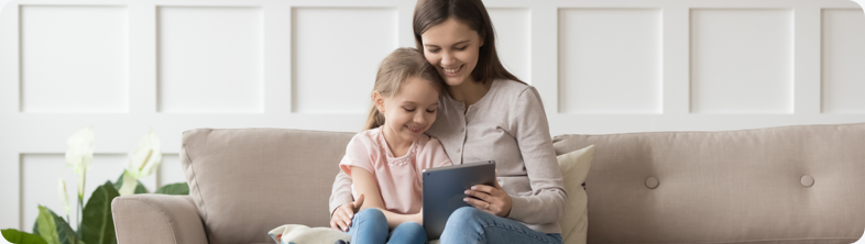 A woman sits on the couch with her daughter and checks her credit score on her tablet