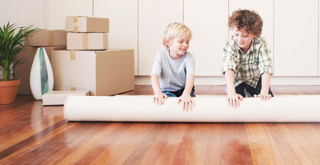 two kids help move by rolling up a carpet